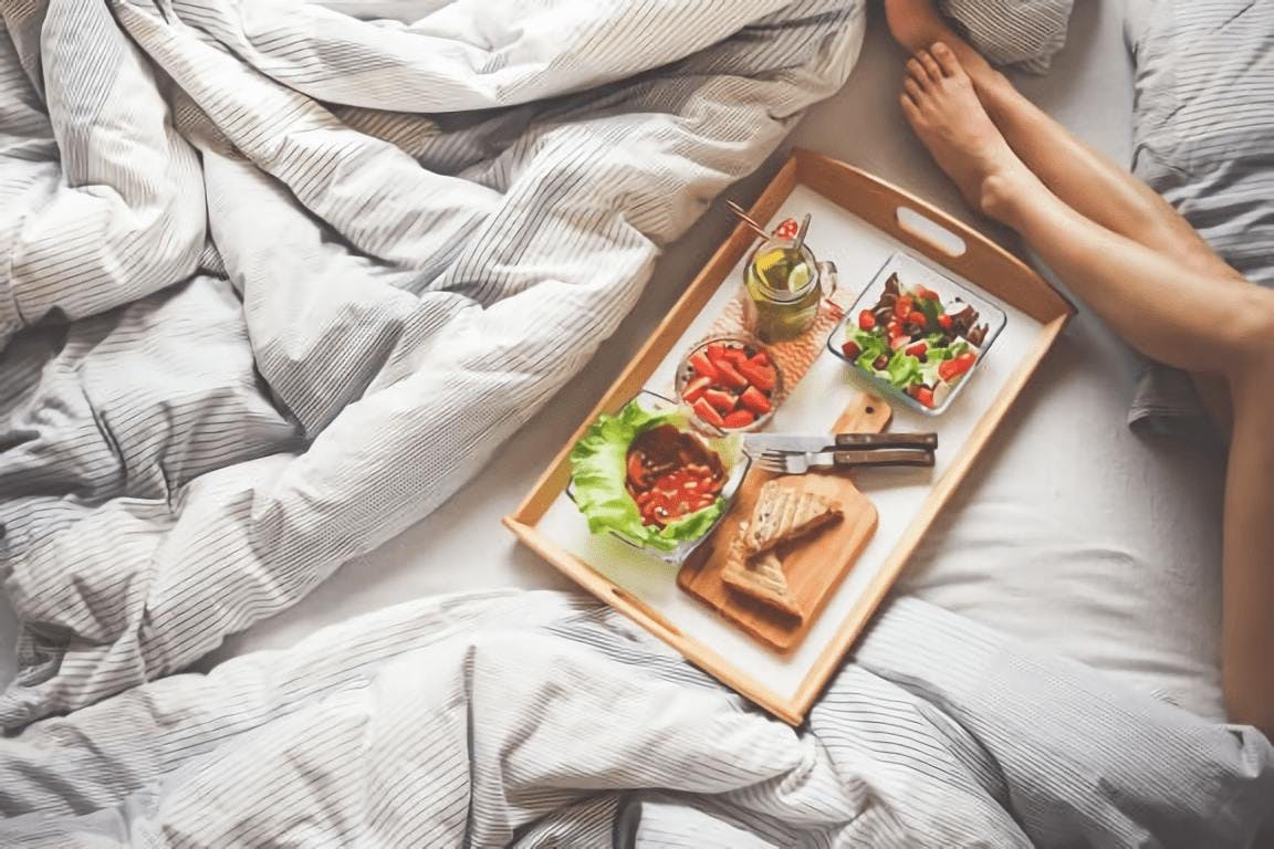 piernas de mujer en cama con bandeja con desayuno